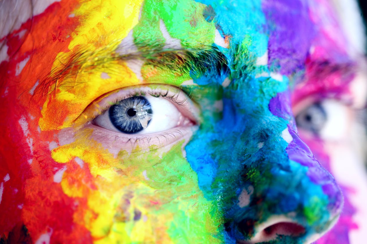 about-us-02 Close-up of a person with colorful rainbow face paint, symbolizing LGBT pride and expression.